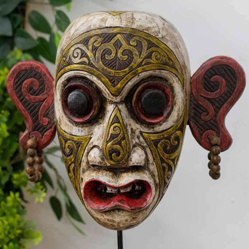 Máscara tribal artesanal da região de Kalimantan, Bornéu, esculpida em madeira com padrões étnicos em vermelho, preto e dourado.