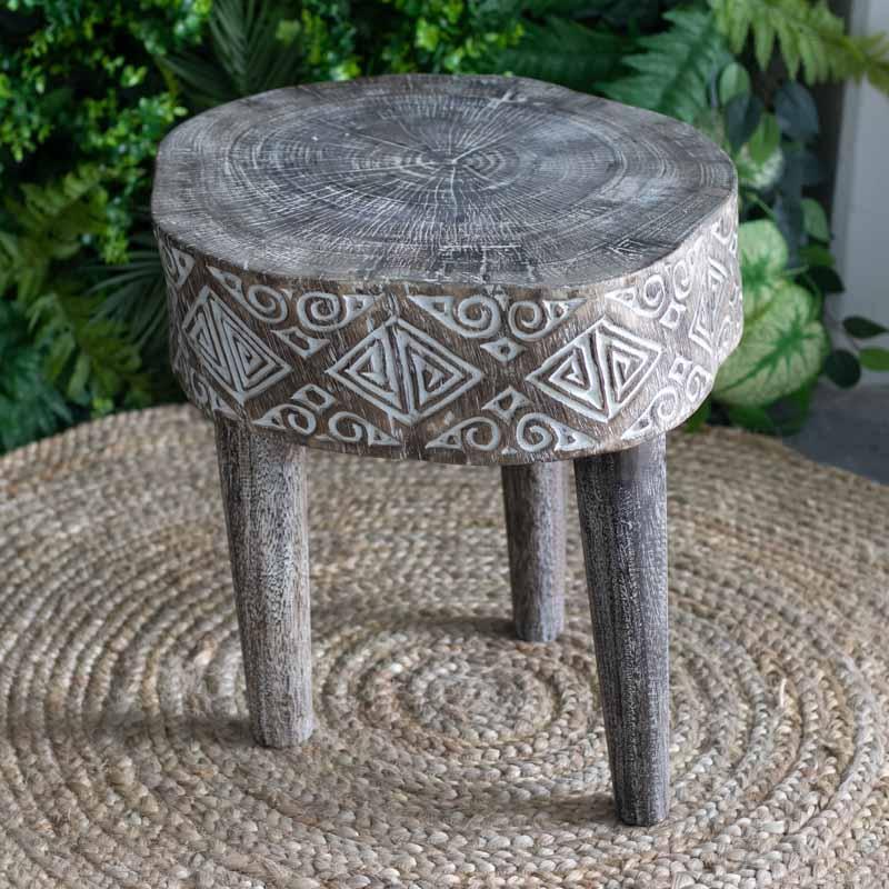 Detalhe lateral de mesa de apoio redonda com grafismos primitivos esculpidos à mão, destacando a cultura da Indonésia.