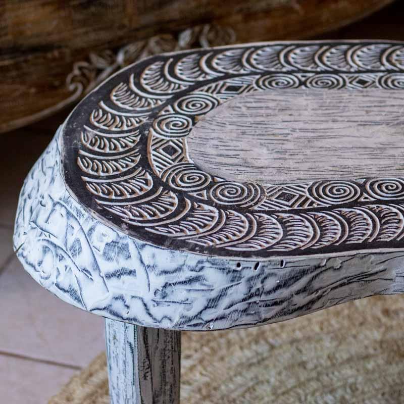 Mesa de centro artesanal em madeira maciça de Timor com formato orgânico e ricos entalhes tribais em pátina branca.