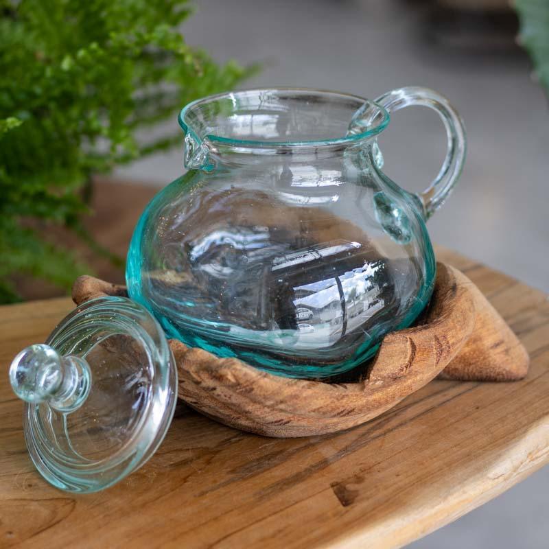 Jarra artesanal com tampa apoiada sobre mãos esculpidas em madeira.