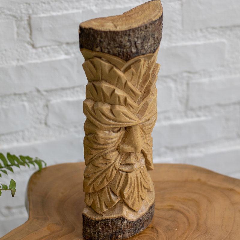 Arte em madeira com expressão simbólica do Green Man sobre tronco natural.