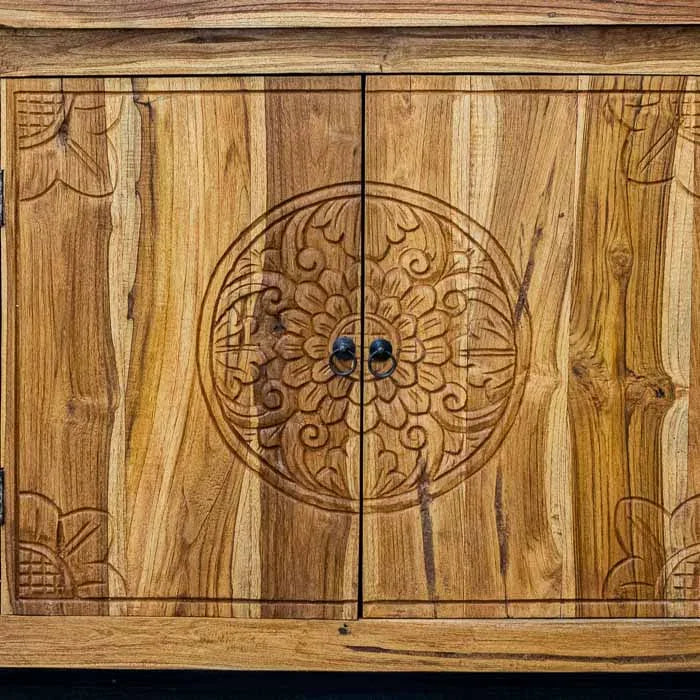Detalhe do trabalho manual balinês em madeira teca, destacando os relevos botânicos do gabinete.