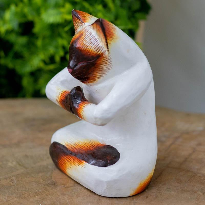 Detalhe frontal de gato místico esculpido em madeira, exibindo uma expressão facial serena com olhos fechados e focinho detalhado.