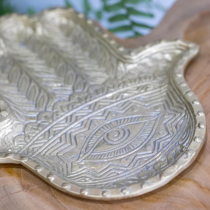 Detalhe do Olho Grego central e padrões geométricos entalhados em bandeja de bronze artesanal.