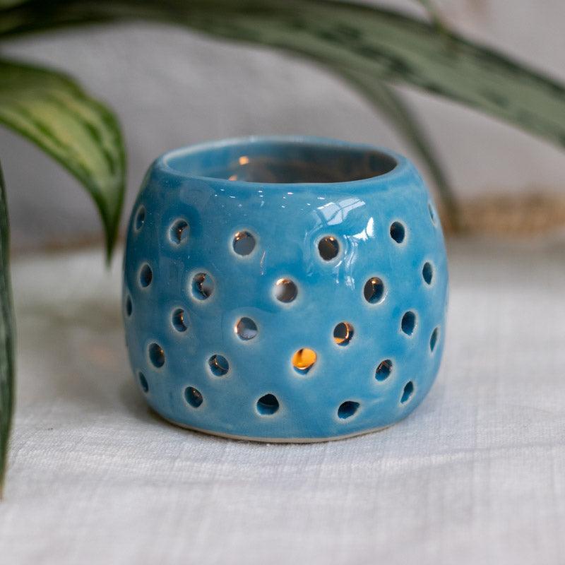 Porta-velas de cerâmica azul com furos circulares e vela acesa