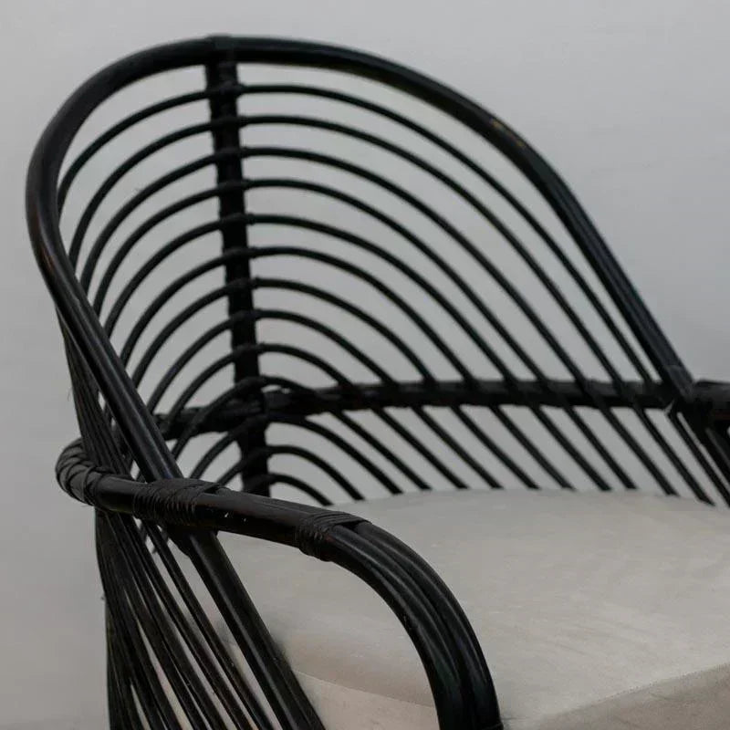 Poltrona artesanal de rattan natural pintada de preto com assento estofado branco, destacando o design curvilíneo de Bali.