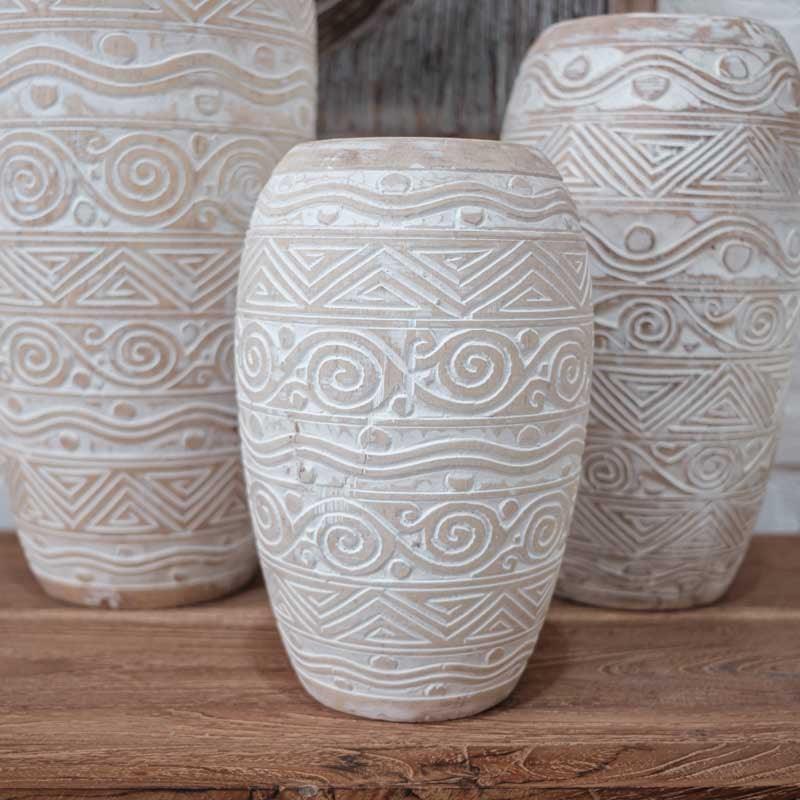 Nesta foto, o Vaso em Madeira Pátina Étnico | Bali está elegantemente exibido em um cenário de sala de estar, criando um ponto focal exótico e atraente. A iluminação suave realça os tons da madeira e a pátina, criando uma atmosfera acolhedora e convidativa.