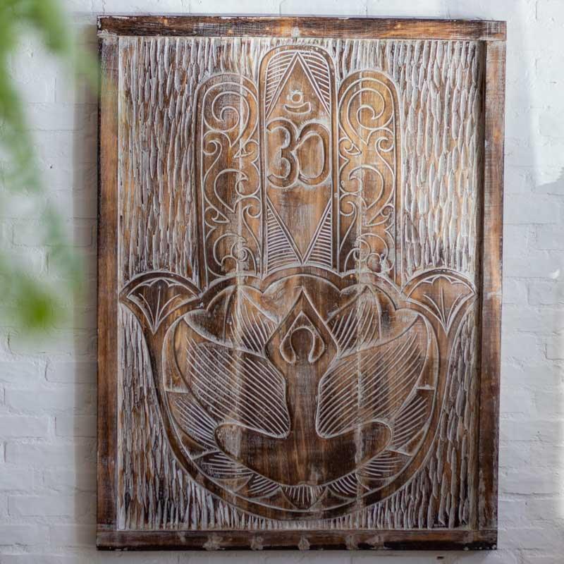 Painel artesanal em madeira natural produzido em Bali, com relevos delicados da Hamsá e símbolo Om, ideal para decorações com inspiração espiritual e zen.