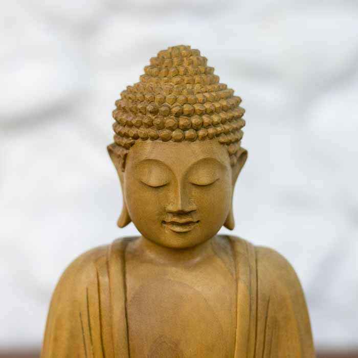 Estatueta decorativa balinesa do Buda em meditação com mãos sobrepostas no colo esculpida em madeira clara.