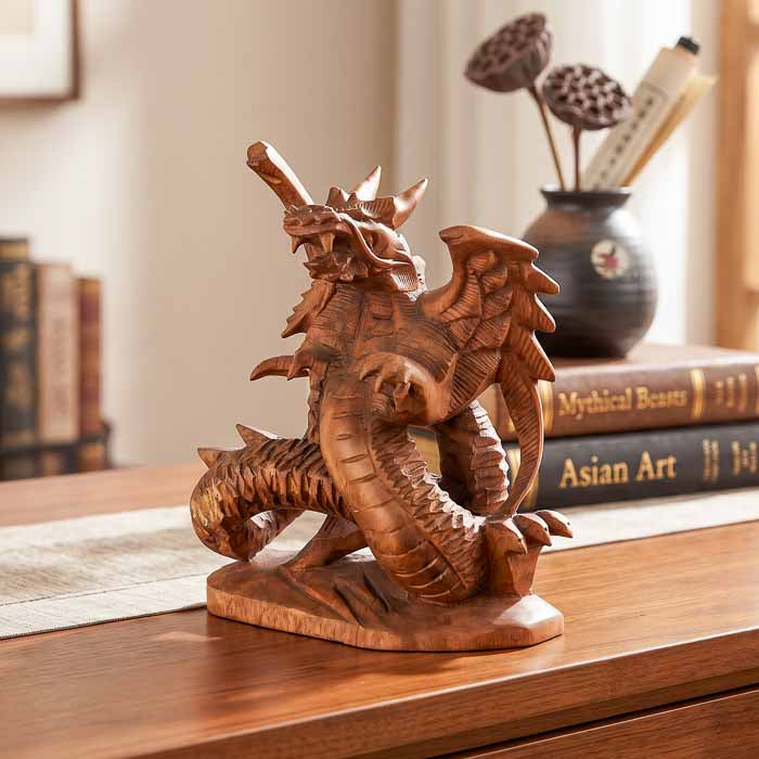 Escultura artesanal de dragão alado em madeira de Teca maciça entalhada sobre mesa com livros ao fundo.