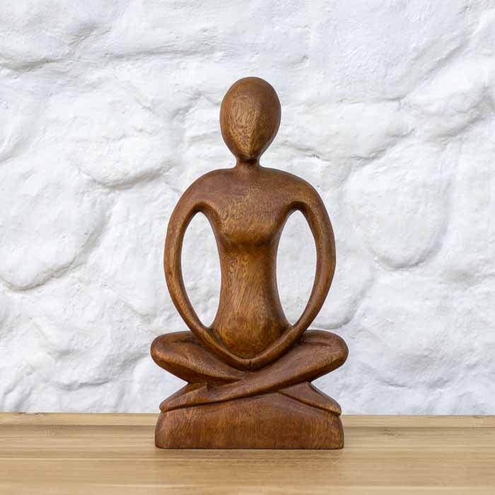 Escultura artesanal de yogi em meditação na posição de lótus esculpida em madeira de Teca maciça sobre mesa.
