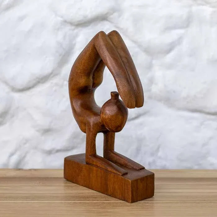 Estatueta feita à mão, obra abstrata de praticante de ioga na Postura do Escorpião em madeira maciça sobre mesa de madeira.