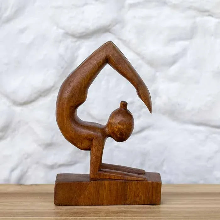 Escultura artesanal abstrata da praticante de ioga na Postura do Escorpião em madeira maciça sobre mesa de madeira.