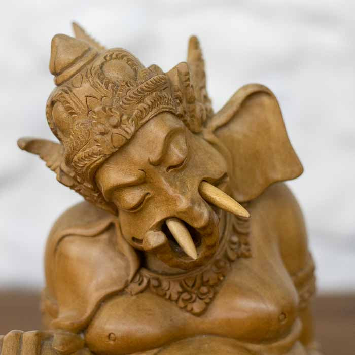 Estatueta decorativa balinesa do Deus Ganesh com coroa entalhada e expressão serena esculpida em madeira clara.