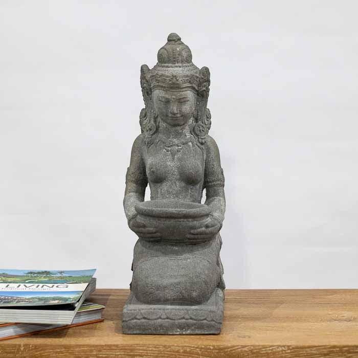 Escultura artesanal da Deusa Dewi Sri ajoelhada, segurando recipiente para oferendas.