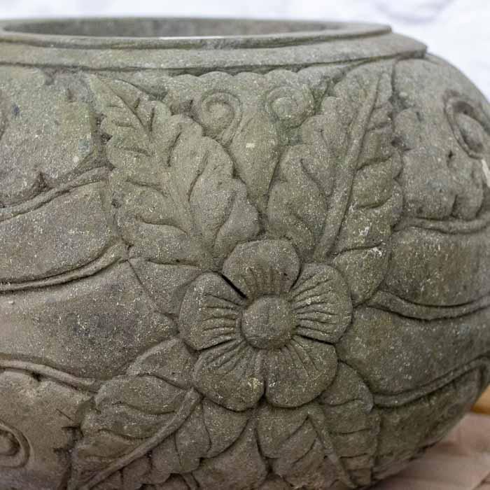 Detalhe da textura porosa e dos desenhos botânicos em vaso de pedra natural de Bali.