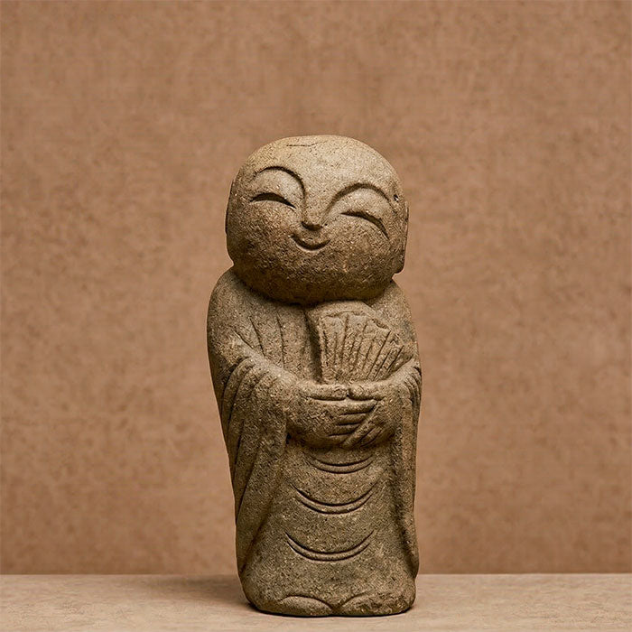 Escultura zen de monge segurando um leque com expressão de alegria e paz interior.