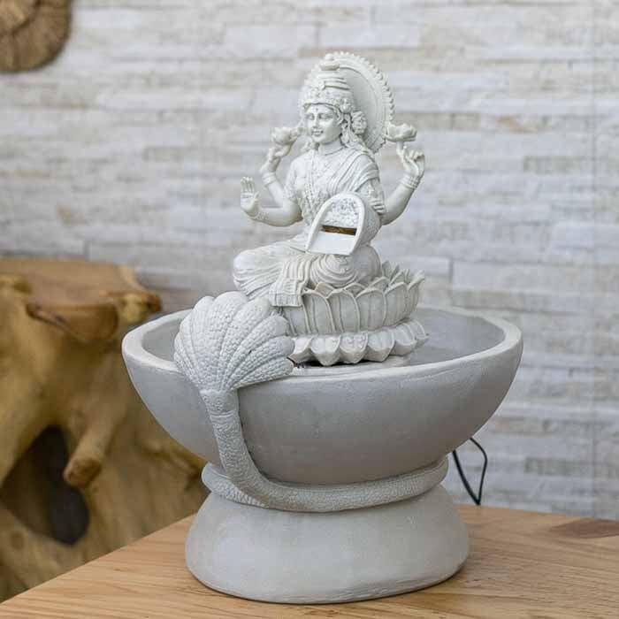 Imagem de Lakshmi sentada em lótus com luz interna refletindo no movimento da água da fonte artesanal.