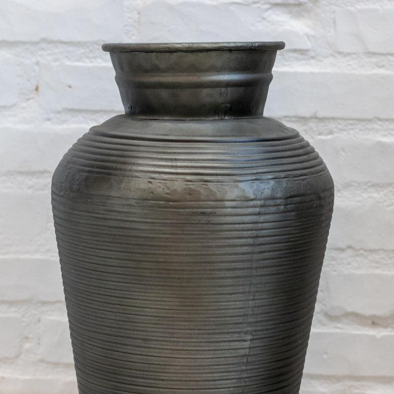 Urna decorativa de metal de 45cm com design esguio e textura linear em ambiente de decoração moderna.