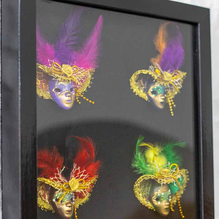 Composição artística com máscaras de gala italianas e penas vibrantes de pavão e avestruz em fundo escuro.