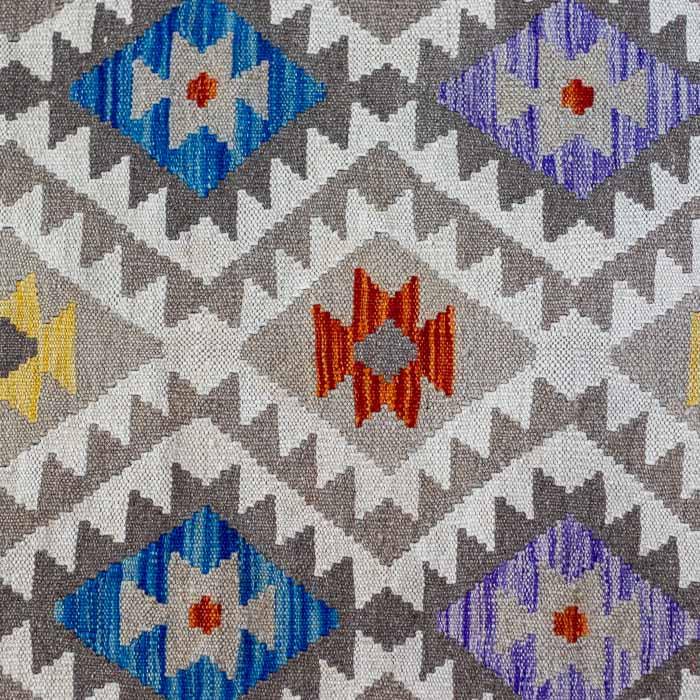 Tapete artesanal Kilim do Paquistão com padrão geométrico de diamantes coloridos em trama plana manual sobre piso de madeira.