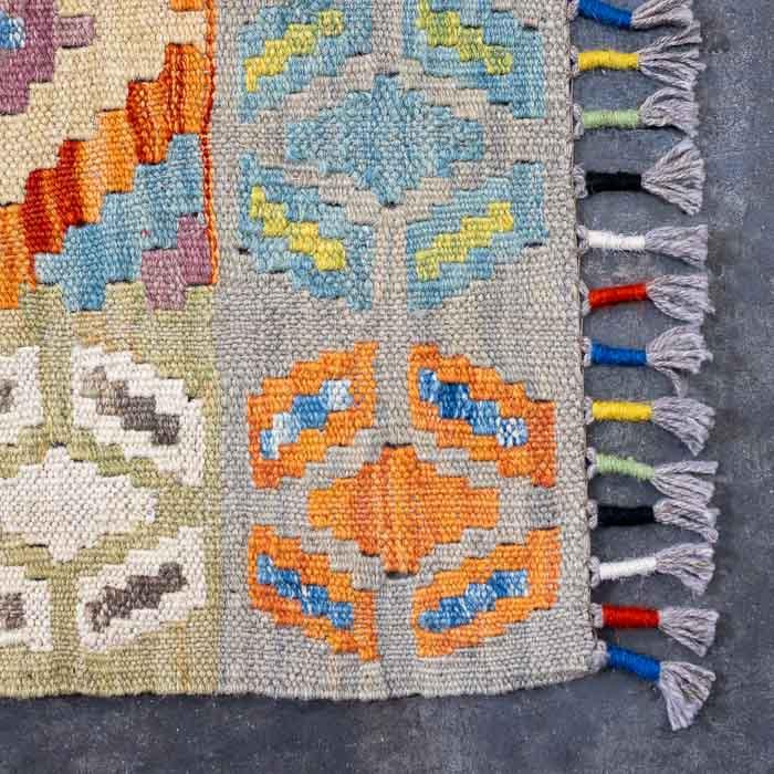 Detalhe da trama firme de passadeira artesanal colorida destacando losangos ancestrais e acabamento manual em franjas.