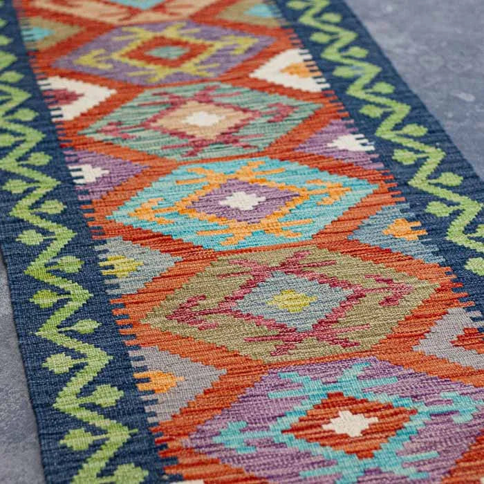 Detalhe da trama firme e colorida de passadeira Kilim artesanal destacando losangos étnicos ancestrais e acabamento em franjas.