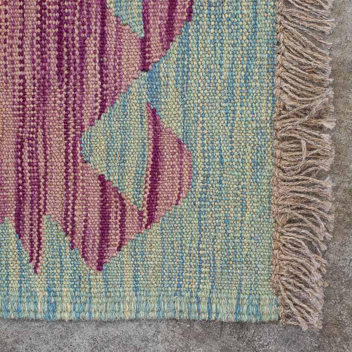 Detalhe da textura firme da lã natural em passadeira colorida destacando padrões ancestrais e acabamento artesanal em franjas.