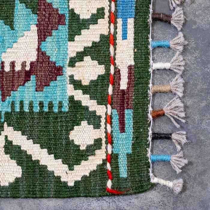 Detalhe da trama firme de tapete artesanal colorido destacando padrões ancestrais e acabamento manual em franjas.