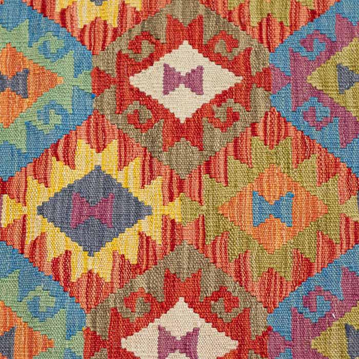 Detalhe da trama firme e colorida de tapete afegão legítimo em tons de terracota, azul e amarelo.