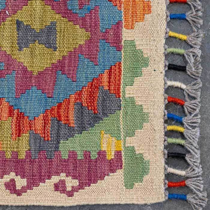Vista superior de passadeira Kilim artesanal destacando a simetria dos padrões tribais e a vibração das cores.