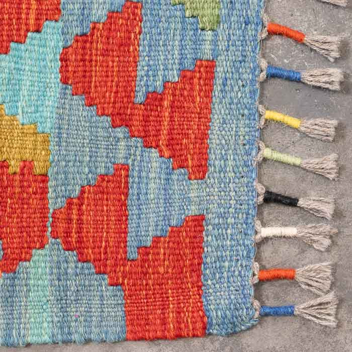 Detalhe da tecelagem manual firme de tapete colorido destacando padrões ancestrais em lã e acabamento artesanal em franjas.