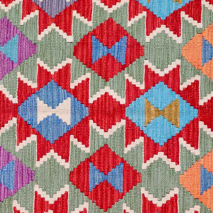 Tapete artesanal Kilim do Afeganistão apresentando grafismos étnicos simétricos sobre trama manual plana de lã natural.