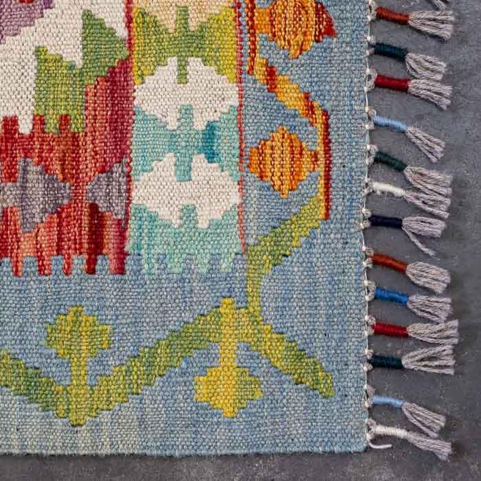 Detalhe da tecelagem manual firme de tapete colorido destacando padrões ancestrais e acabamento artesanal em franjas.