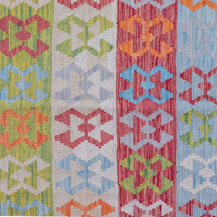 Tapete colorido artesanal kilim do Afeganistão com padrões geométricos tribais sobre piso cinza.