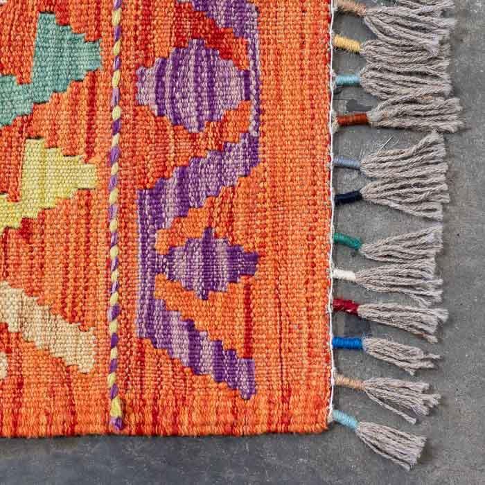 Detalhe da tecelagem manual firme de tapete colorido destacando padrões ancestrais e acabamento artesanal em franjas.