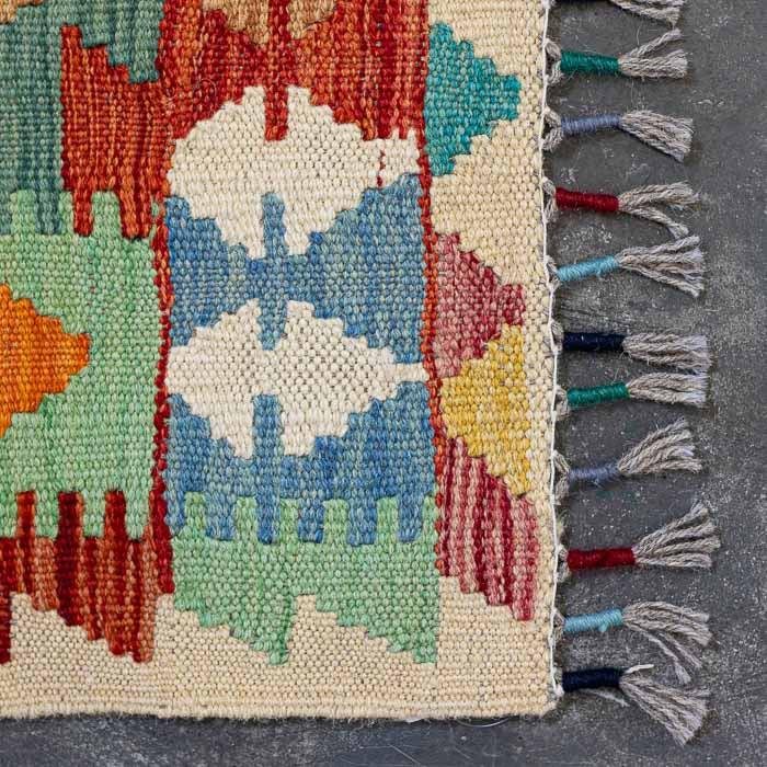 Detalhe da tecelagem manual firme de tapete colorido destacando padrões ancestrais e acabamento artesanal em franjas.