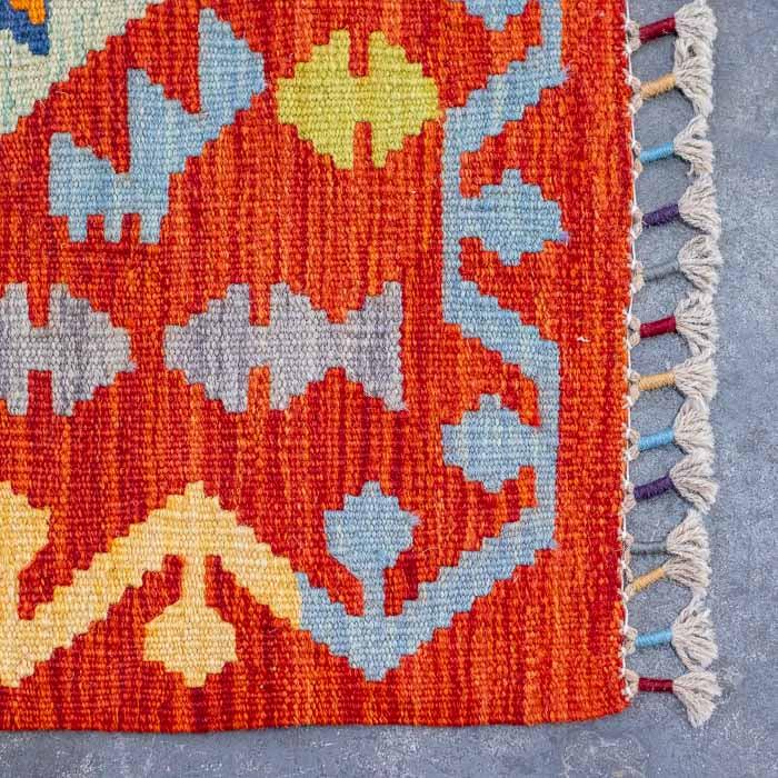 Tapete Kilim afegão de 300cm estendido sobre piso de cimento queimado.