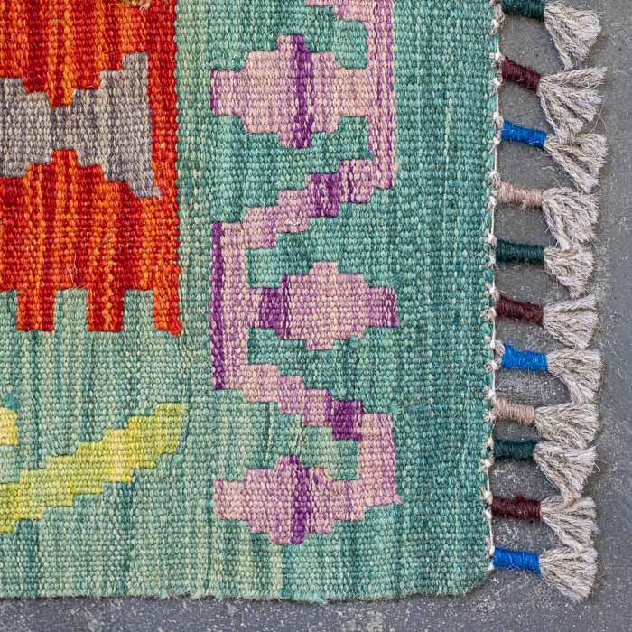 Detalhe da tecelagem manual firme de tapete colorido destacando padrões ancestrais e acabamento artesanal em franjas.