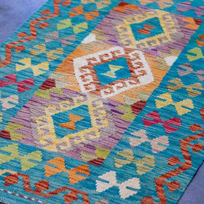 Kilim afegão de 127cm com cores vibrantes e design orgânico sobre piso escuro.