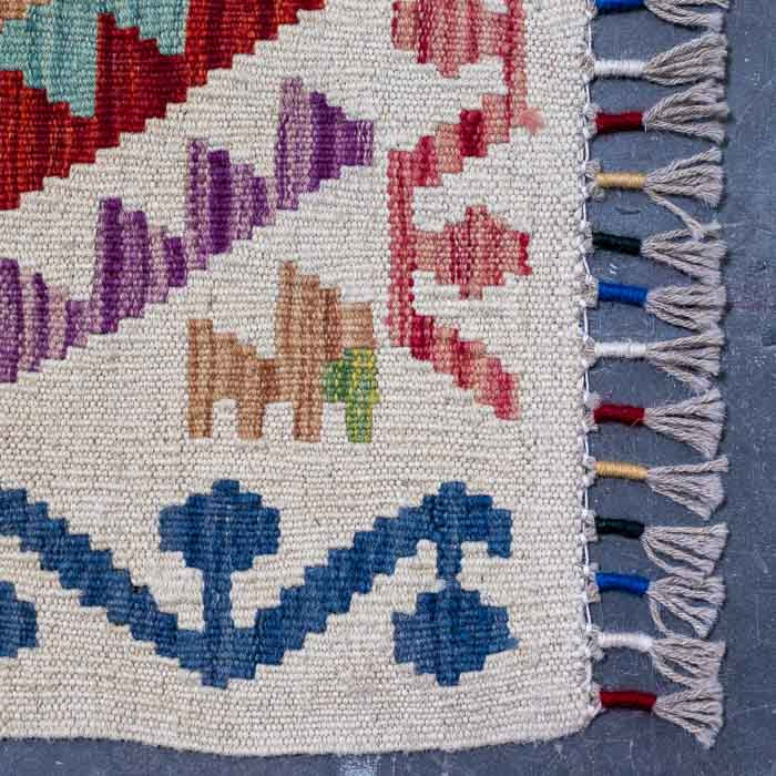 Detalhe da superfície firme do tapete colorido destacando losangos étnicos e acabamento manual em franjas.