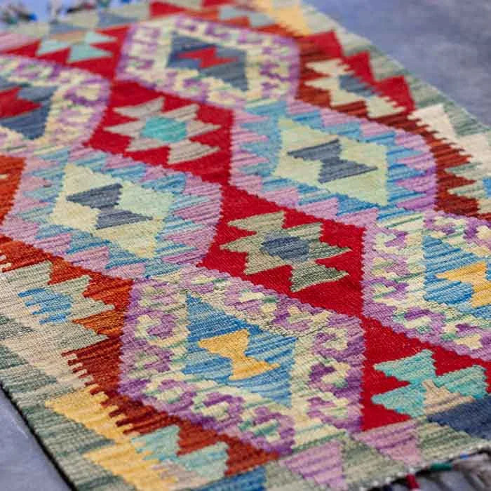 Kilim afegão de 97cm com design orgânico sobre superfície de cimento queimado.