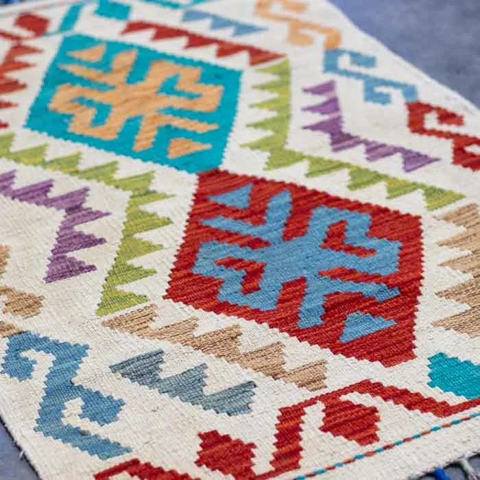 Tapete estilo étnico com desenhos geométricos vibrantes e franjas coloridas manuais.