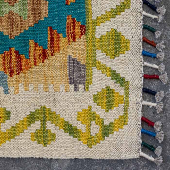 Detalhe da trama firme e colorida de passadeira Kilim artesanal destacando losangos étnicos e acabamento em franjas.