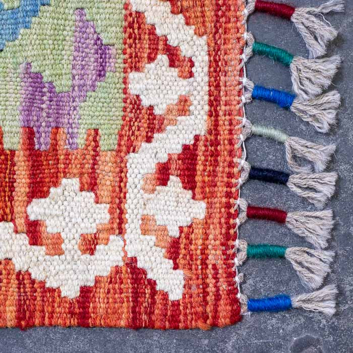 Detalhe da trama firme de tapete artesanal colorido destacando padrões ancestrais e acabamento manual em franjas.