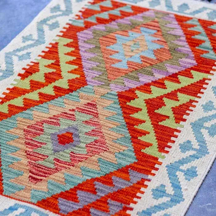 Tapete estilo étnico com desenhos geométricos vibrantes e franjas coloridas manuais.