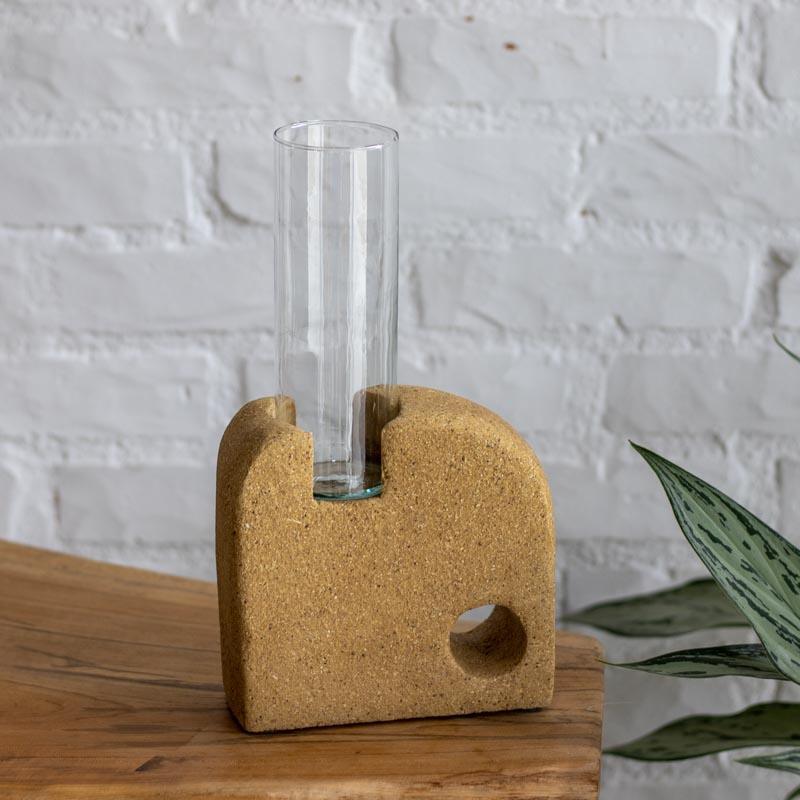 Vaso escultura em cerâmica reciclada bege com textura de serragem de madeira e cilindro de vidro centralizado.