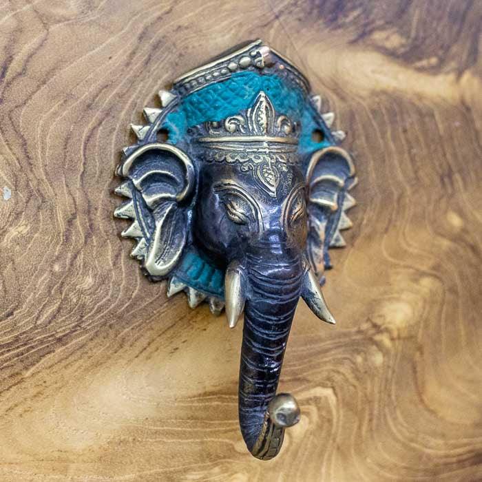 Detalhe do puxador de porta em bronze com imagem de Ganesha em relevo dourado e pátina verde, representando o trabalho artesanal balinês e o simbolismo hindu. 