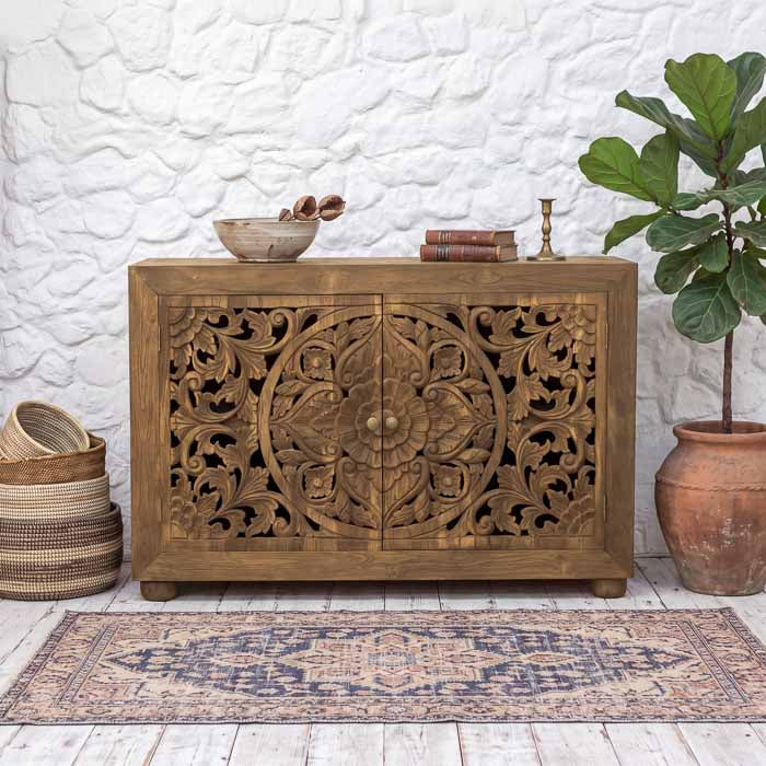 Gabinete floral artesanal em madeira de demolição balinesa com duas portas entalhadas em mandala floral sobre tapete decorativo.
