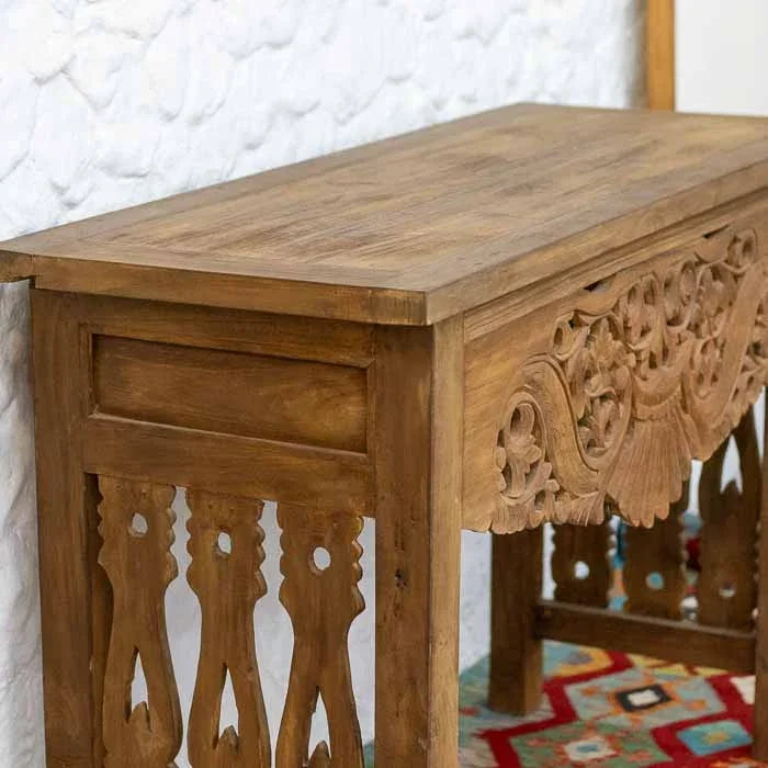 Mesa aparador rústica de Bali em madeira de demolição com entalhes florais vazados em parede de pedra branca.
